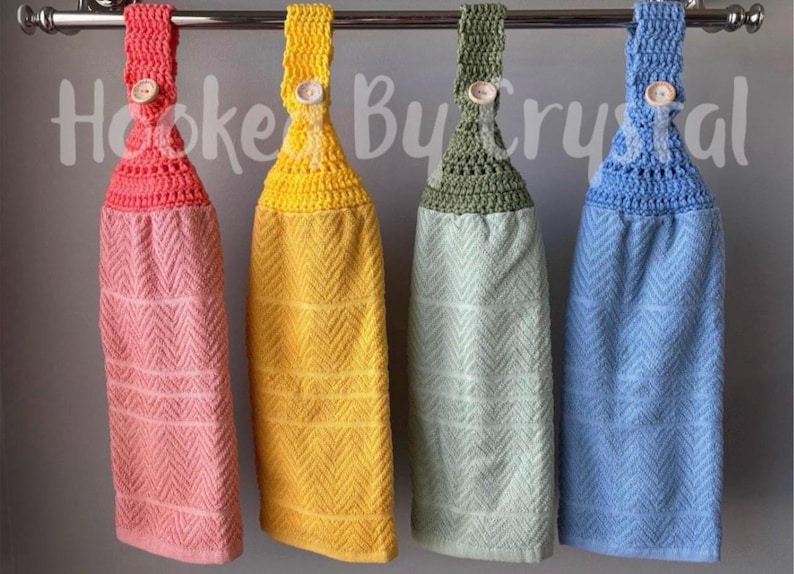 Pode incluir: Quatro toalhas de cozinha suspensas com partes superiores em croch&ecirc; nas cores coral, amarelo, verde s&aacute;lvia e azul claro. Cada toalha apresenta uma textura em espinha de peixe e um fecho de bot&atilde;o de madeira na al&ccedil;a de croch&ecirc;. O texto Hooked By Crystal &eacute; vis&iacute;vel.
