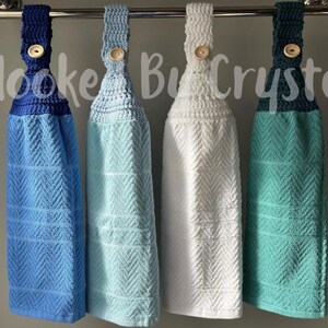 Pode incluir: Quatro toalhas de cozinha suspensas com partes superiores em croch&ecirc; nas cores azul marinho, azul claro, branco e verde-azulado. Cada toalha apresenta uma textura em espinha de peixe e um fecho de bot&atilde;o de madeira. O texto Hooked By Crystal &eacute; vis&iacute;vel.