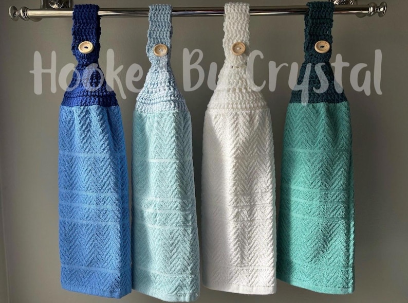 Pode incluir: Quatro toalhas de cozinha suspensas com partes superiores em croch&ecirc; nas cores azul marinho, azul claro, branco e verde-azulado. Cada toalha apresenta uma textura em espinha de peixe e um fecho de bot&atilde;o de madeira. O texto Hooked By Crystal &eacute; vis&iacute;vel.