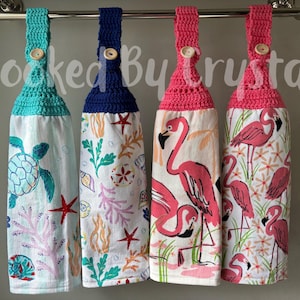 May include: Four hanging kitchen towels with crochet tops and wooden buttons. The towels feature sea turtle, starfish, coral, and flamingo designs. The text "Hooked By Crystal" is visible in the background.