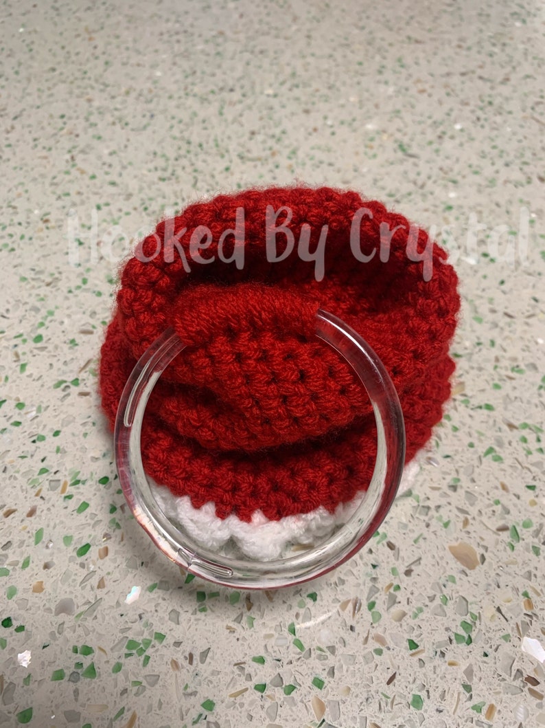 Puede incluir: Un gorro de Pap&aacute; Noel de punto rojo con ribete blanco, que tiene un anillo de pl&aacute;stico transparente unido al borde.