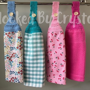 Pode incluir: Quatro toalhas de cozinha penduradas com topos de croch&ecirc; em azul, azul-petr&oacute;leo, rosa claro e rosa escuro, cada uma presa com um bot&atilde;o de madeira. As toalhas apresentam padr&otilde;es florais, xadrez e de cerejas, com uma toalha texturizada lisa. Texto Hooked By Crystal.