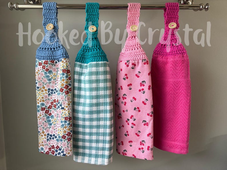 Pode incluir: Quatro toalhas de cozinha penduradas com topos de croch&ecirc; em azul, azul-petr&oacute;leo, rosa claro e rosa escuro, cada uma presa com um bot&atilde;o de madeira. As toalhas apresentam padr&otilde;es florais, xadrez e de cerejas, com uma toalha texturizada lisa. Texto Hooked By Crystal.