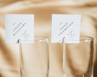 May include: Two champagne flutes with place cards for a wedding reception. The place cards are white with black text and read "Mr. & Mrs. Chloe Williams" and "Mr. & Mrs. Noah Thompson".