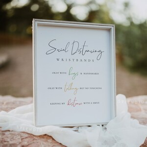 Può includere: Un cartello bianco con testo nero che recita "Social Distancing Wristbands". Il cartello elenca tre livelli di distanziamento sociale: ok con abbracci e strette di mano, ok con parlare ma senza toccare, e mantenendo le distanze con un sorriso.