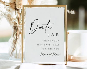 May include: A gold-framed sign with the text "Date Jar" in black cursive script. The sign also includes the text "Share your best date ideas for the new Mr. and Mrs."