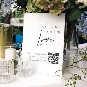 May include: White sign with black text that reads "Capture the Love" with a camera icon. Below the text is a QR code and the text "Please share your photos with us. Scan and upload!"