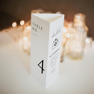 May include: White triangular table number card with black text. The card says "Table No." and "4". It also has a camera icon and the text "photo booth" and "#lilvandrenji! Please share your photos & videos, tag us with our hashtag".