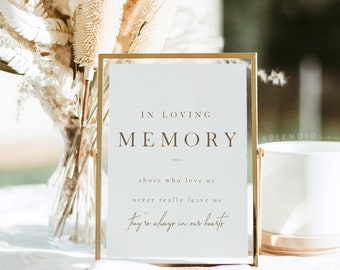May include: A white sign with a gold frame, sitting on a table with dried flowers. The sign reads "In Loving Memory" with the text "Those who love us never really leave us. They're always in our hearts."
