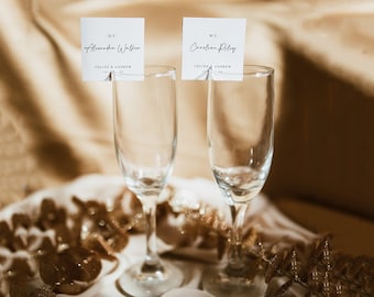 May include: Two champagne flutes with place cards. The cards are white with black text and say "Ms. Alexandra Walker" and "Ms. Caroline Riley".