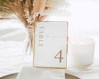 May include: A gold-framed table number card with the word "TABLE" and the number "4" printed in brown on a white background.