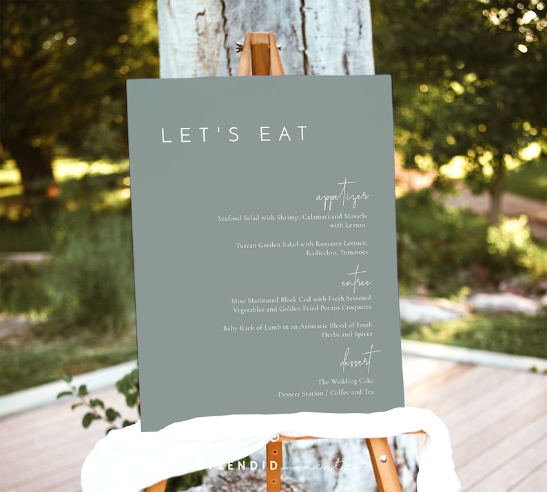May include: A light green sign with the text "LET'S EAT" in white. The sign lists a wedding menu with starters, main courses, and desserts. The starters include Seafood Salad and Tuscan Garden Salad. The main courses include Miso Marinated Black Cod and Baby Rack of Lamb. The dessert is The Wedding Cake.