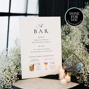 May include: A white rectangular bar menu sign with black text listing beer, wine, and signature cocktails including Grapefruit Bourbon Sour and Mango Sidecar. The sign features illustrations of the two cocktails and the text DONE FOR YOU.