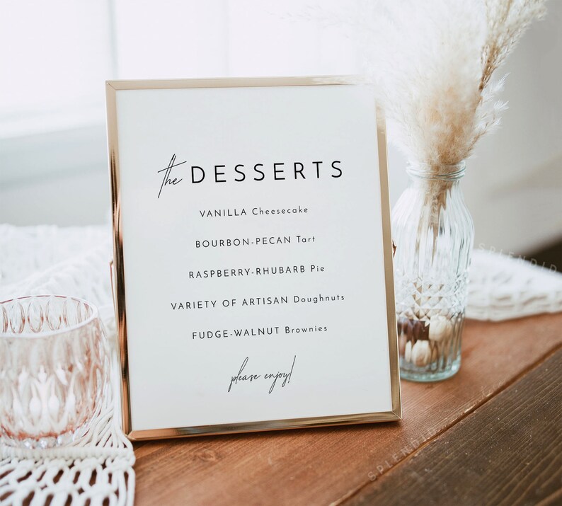 May include: A gold-framed sign with the word "DESSERTS" in cursive script. The sign lists a variety of desserts, including vanilla cheesecake, bourbon-pecan tart, raspberry-rhubarb pie, artisan doughnuts, and fudge-walnut brownies. The sign ends with the phrase "please enjoy!"