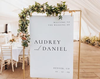 May include: A white sign with a gold frame and greenery garland on top. The sign reads "Welcome to the wedding of Audrey and Daniel, Denver, CO 10.12.20".