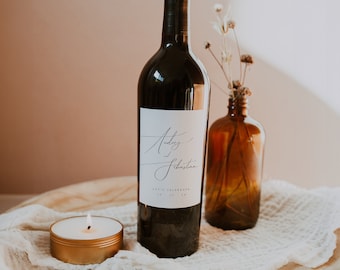 May include: A bottle of red wine with a white label that says "Audrey & Sebastian Let's Celebrate" on a wooden tray with a white cloth and a small candle.