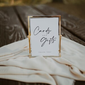 May include: A gold-framed sign with a white background and black text that reads "Cards and Gifts" with the words "Thank You!" at the bottom.