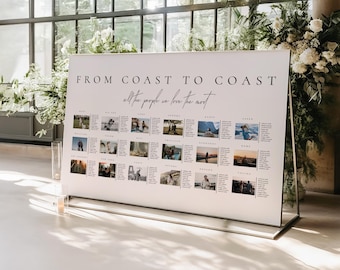 May include: A white sign with the text "FROM COAST TO COAST all the people we love the most" in black. The sign has a mirrored base and features small photos arranged in rows. The sign is displayed in front of a large window with floral arrangements.