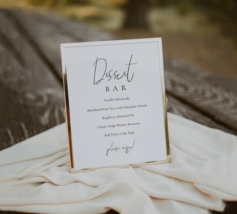 Puede incluir: Un cartel con marco dorado, fondo blanco y texto negro que dice "Dessert Bar". El cartel enumera una variedad de postres, que incluyen pastel de queso de vainilla, tarta de bourbon y nuez pecana con llovizna de chocolate, pastel de frambuesa y ruibarbo, brownies cl&aacute;sicos de fudge y nuez y cake pops de terciopelo rojo. El cartel tambi&eacute;n incluye la frase "&iexcl;por favor, disfruta!"