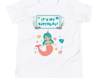 May include: White t-shirt with a mermaid illustration and the text "It's My Birthday!" on a blue sign. The mermaid has green hair, a pink tail, and a party hat.