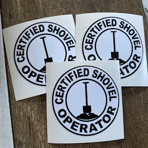 May include: Three white stickers with black text and a black shovel graphic. The text on the stickers reads "Certified Shovel Operator".