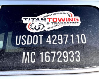 May include: A white sticker on a black background with the text "TITAN TOWING & TRANSPORT" in a red and white circle with a chain link design. Below the sticker is the text "USDOT 4297110 MC 1672933".