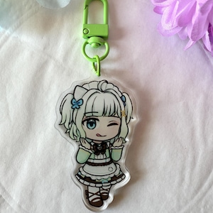 May include: A clear acrylic keychain featuring a cartoon anime girl with white hair, blue eyes, and a wink. The girl is wearing a green and white outfit. The keychain has a green clasp.