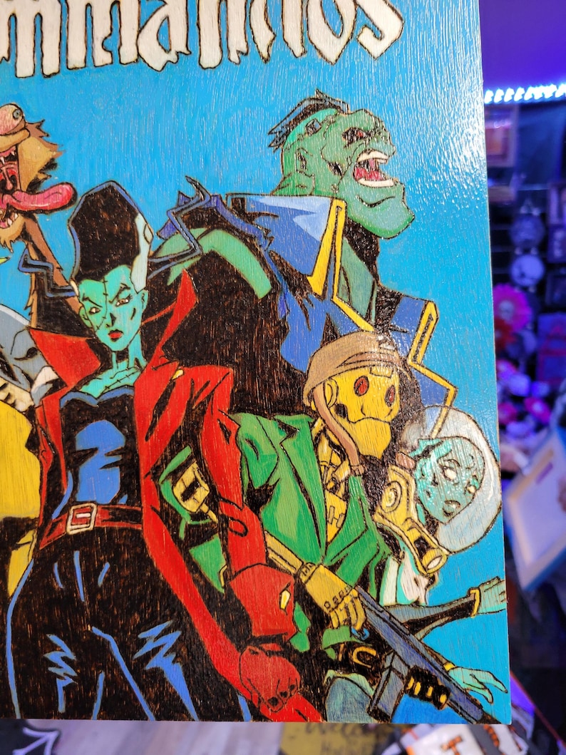 May include: A wood-burned illustration of a group of cartoon characters. The characters are a green monster with a large mouth, a woman with black hair and green skin, a yellow robot with a helmet, and a blue alien with a helmet. The background is blue.