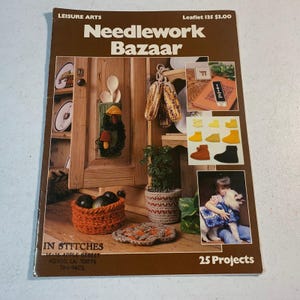 May include: A vintage "Needlework Bazaar" booklet featuring various crochet projects. The cover showcases a variety of handmade items, including a basket, coasters, and decorative corn. The booklet is from Leisure Arts and includes the text "25 Projects".