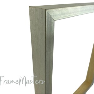 May include: Close-up of a silver picture frame with a wood backing. The frame has a smooth, metallic finish and a simple, rectangular design.