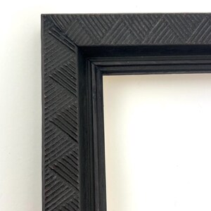 May include: A black picture frame with a decorative, carved, geometric pattern on the outer edge.