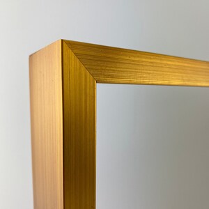 May include: Close-up of the corner of a gold picture frame. The frame has a brushed metal finish.