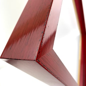 May include: Close-up of a red wooden picture frame with a distressed finish. The frame is angled and the edges are visible.