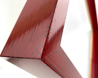 May include: Close-up of a red wooden picture frame with a distressed finish. The frame is angled and the edges are visible.