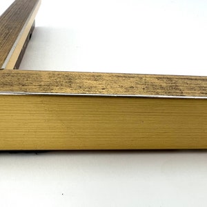 Puede incluir: Primer plano de un marco de imagen dorado con un acabado de madera desgastada. El marco tiene un fino borde plateado.