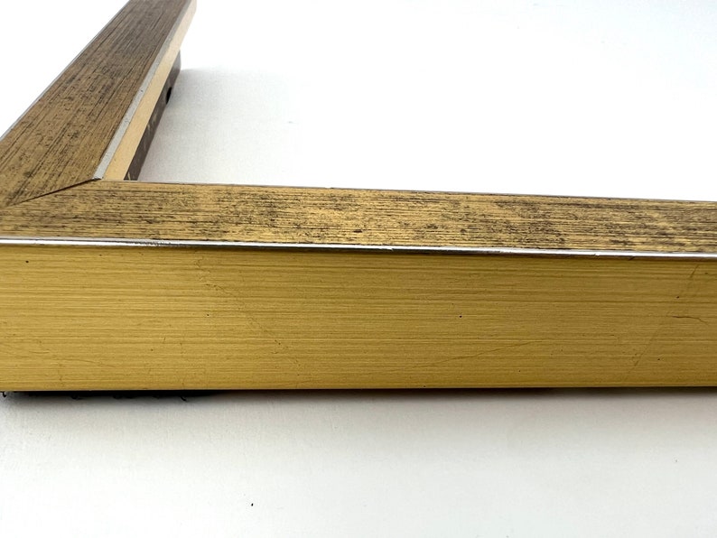 Puede incluir: Primer plano de un marco de imagen dorado con un acabado de madera desgastada. El marco tiene un fino borde plateado.