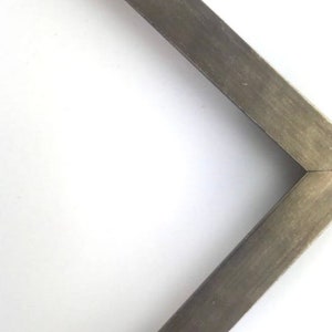 May include: A close-up of a corner of a picture frame with a dark gray wood finish.