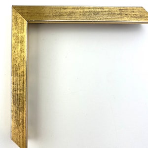 Puede incluir: Una esquina de un marco de imagen dorado con textura de madera.