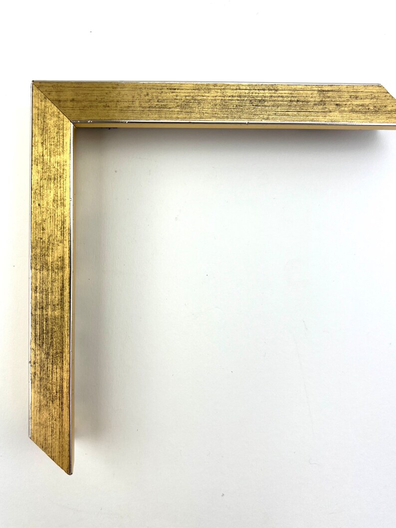 Puede incluir: Una esquina de un marco de imagen dorado con textura de madera.