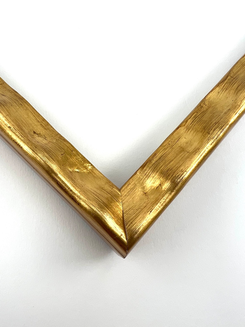 May include: Close-up of a corner of a gold picture frame. The frame has a textured, brushed finish.