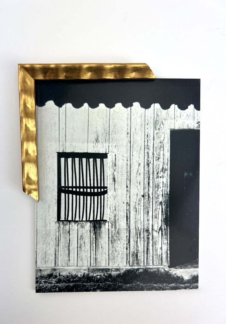May include: Black and white photograph of a wooden building with a window and a door. The building is weathered and has a rustic appearance. The window has a black metal grate.