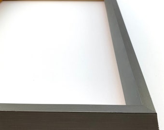 May include: A dark gray picture frame with a wood interior. The frame has a beveled edge and a smooth finish.