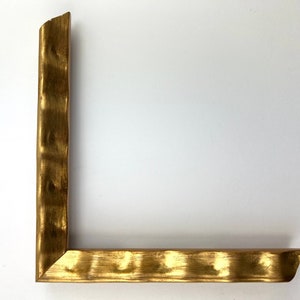 May include: A gold-colored picture frame with a textured, hammered finish. The frame is made of wood and has a simple, rectangular shape.