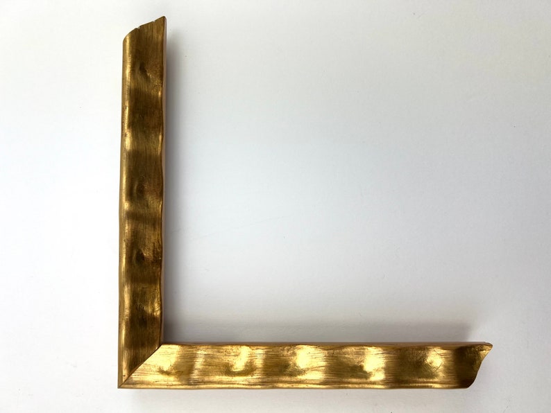 May include: A gold-colored picture frame with a textured, hammered finish. The frame is made of wood and has a simple, rectangular shape.