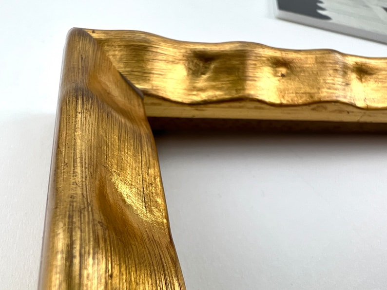 May include: A close-up of a gold-painted picture frame with a wavy, textured design. The frame is made of wood and has a distressed finish.