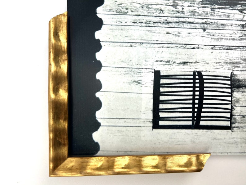 May include: A black and white photograph of a wooden fence with a black metal gate. The photograph is framed in a gold-colored frame with a textured edge.