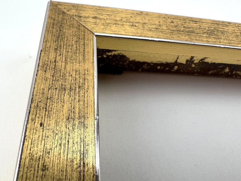 Puede incluir: Un marco de imagen dorado con un borde plateado. El marco tiene una textura de grano de madera y est&aacute; ligeramente desgastado.