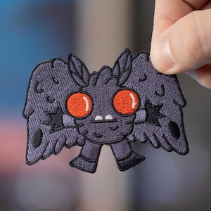 May include: Purple embroidered patch of a cartoon moth with large red eyes and small legs. The moth has a fuzzy, textured appearance.