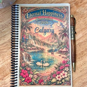 Puede incluir: Un cuaderno con espiral con una colorida portada de estilo vintage que presenta un paisaje tropical con cisnes, cascadas y palmeras. Se muestra el texto "Eternal Happiness Convention 2026 Calgary". Un bolígrafo de madera con detalles metálicos descansa junto al cuaderno.