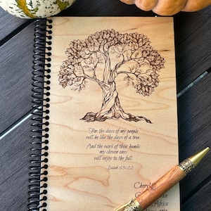May include: A wooden journal with a spiral binding and a tree design burned into the cover. The journal has a quote from Isaiah 65:22, "For the days of my people will be like the days of a tree. And the work of their hands my chosen ones will enjoy to the full." The journal is signed "Cheryl" and dated "March, 1998".
